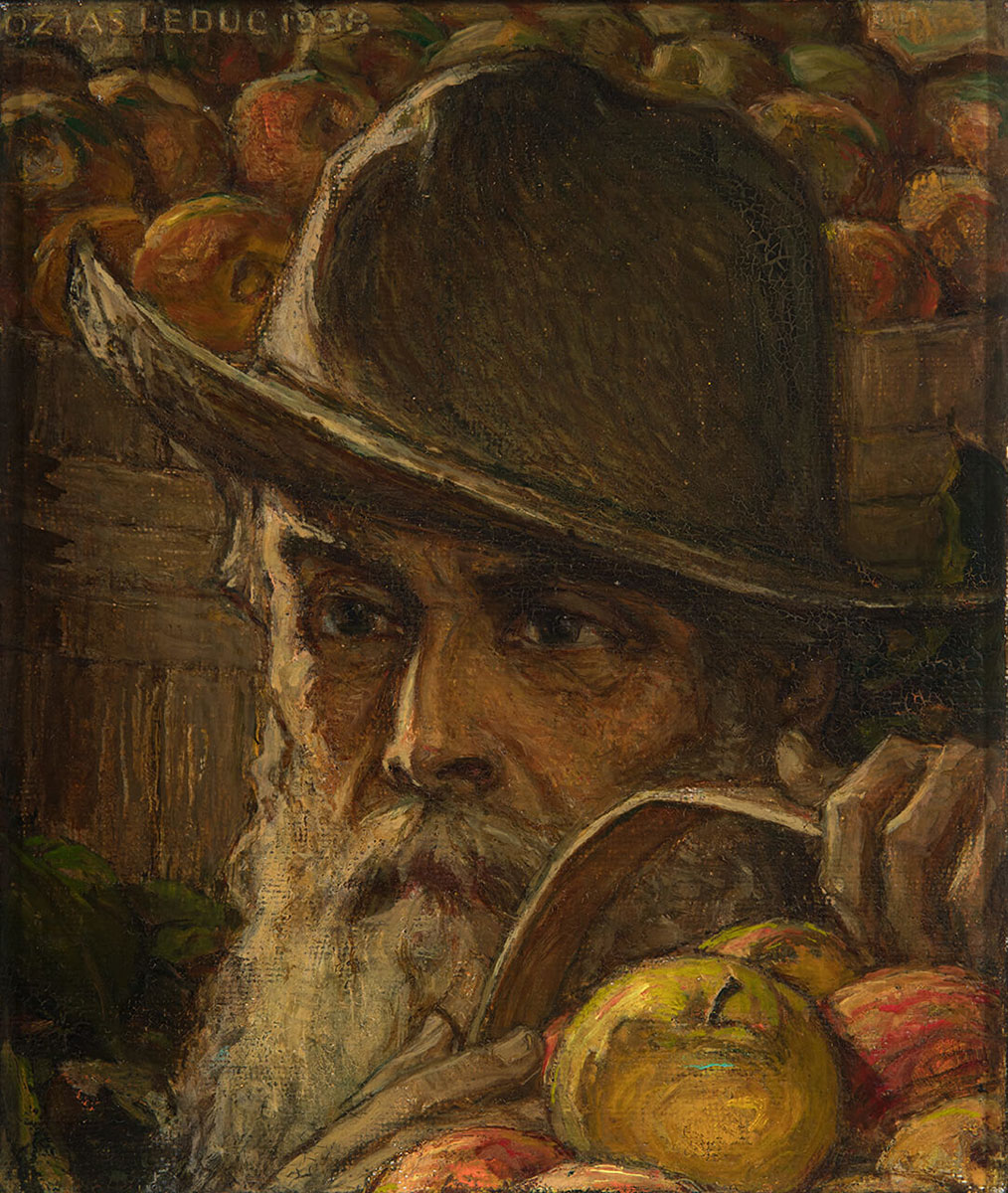 Portrait du père d'ozias Leduc, Antoine, tenant un panier de pommes d'une main, portant un chapeau. Il a une abondante barbe blanche.