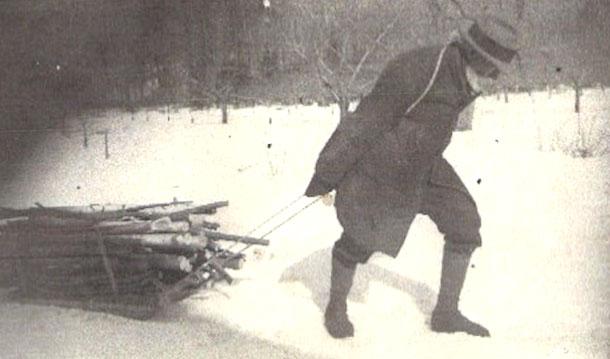 Photo d'Ozias Leduc en hiver tirant derrière lui un traineau rempli de rondins de bois.