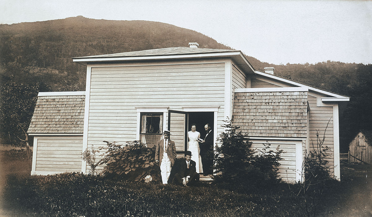 Maison-atelier agrandie, où Leduc ajoute plusieurs pièces à Correlieu. On voit quatre personnes dont Leduc lui-même lisant, devant la porte de la maison avec une montagne à l'arrière.