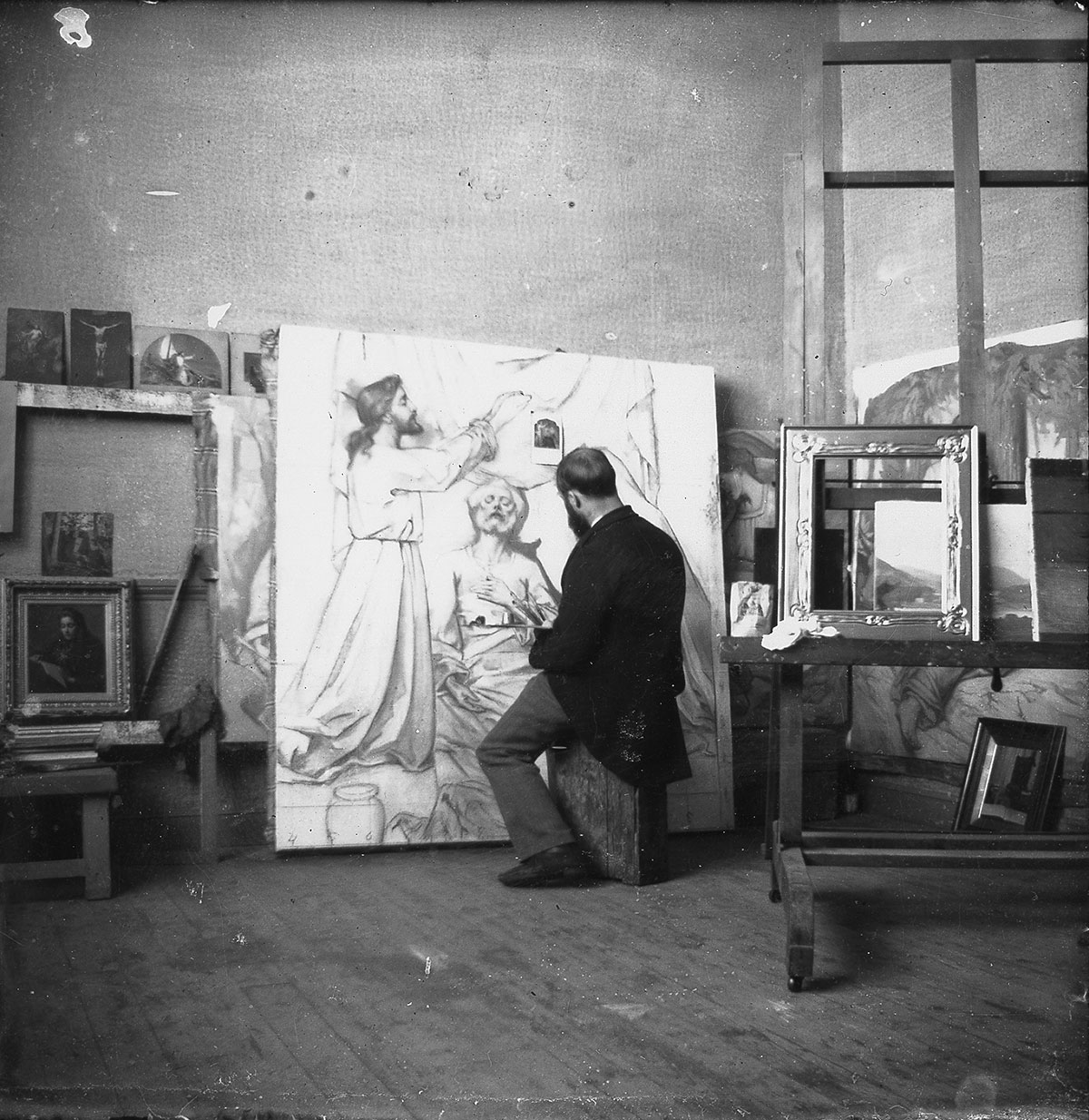 Image montrant Ozias Leduc, assis de dos en train de peindre une scène religieuse.