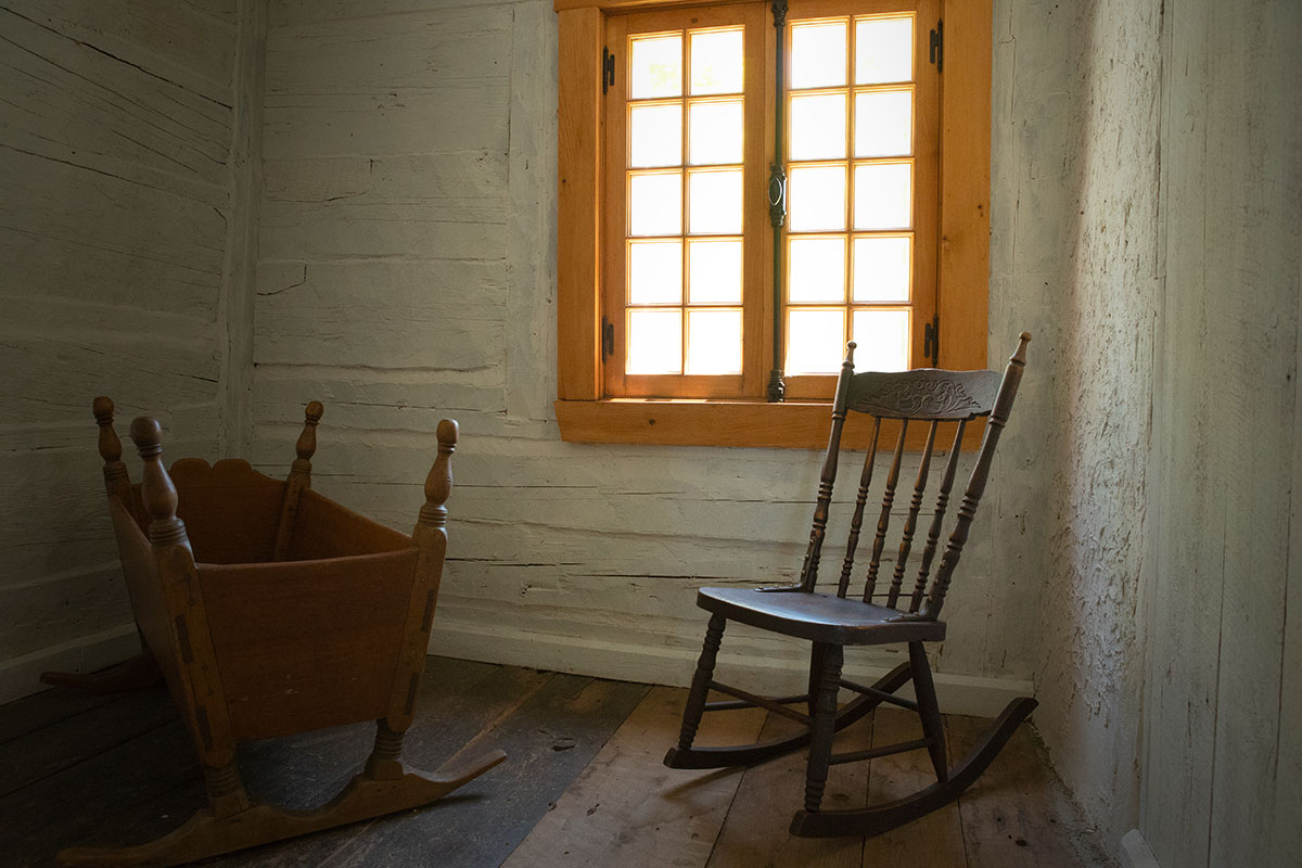Photo montrant une des pièces de la maison natale dans son état actuel. On y voit une chaise berçante et un lit de bébé berçant, devant une fenêtre.