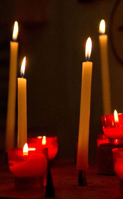 Photo of burning votive candles inside a darkened church.