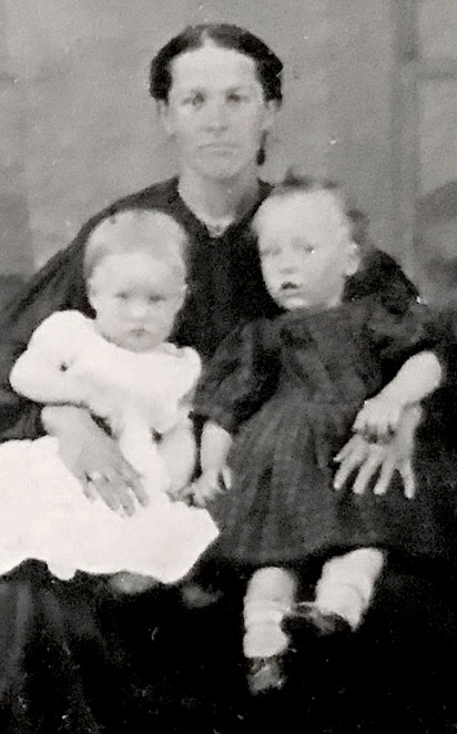 Détail d'une photo d'époque illustrant deux enfants assis sur les genoux de leur mère.