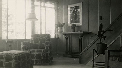 Scene from the video showing a chair, a footstool and a table near the staircase.