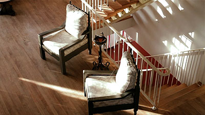 Scene from the video showing the view from the mezzanine of two chairs and the stairs leading to the basement.