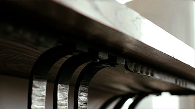 Scène de la vidéo représentant l'attache de la structure en fer forgé à la surface de bois de la table console.